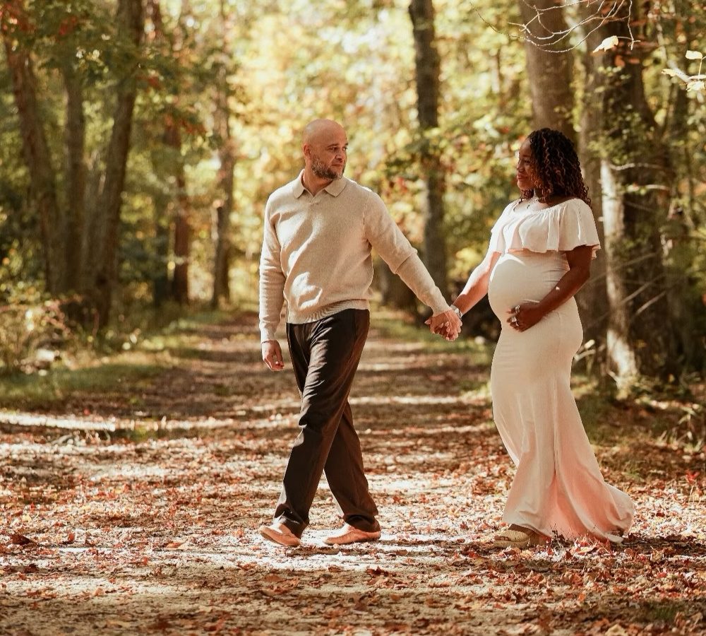 Expecting couple walking hand in hand down a leafy fall path